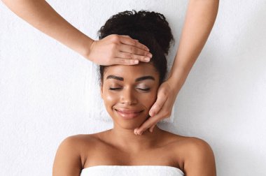 Beyaz arka planda gülümseyen siyahi bayanın yüz masajını kaldırışının en üst görüntüsü. Rahat, Afro-Amerikalı, gözleri kapalı genç bir kadın. Spa 'da yaşlanmayı önleyici yüz prosedürünün tadını çıkarıyor.