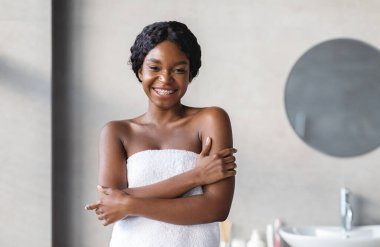 Beyaz havluya bulanmış şehvetli genç bir bayan pürüzsüz tenine dokunuyor, omuzlarına sarılıyor, banyo sonrası ipeksi dokunuşlardan hoşlanıyor, kameraya gülümsüyor, banyo içi, kopyalama alanı.