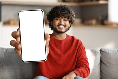 Cep telefonu reklamı. Gülümseyen Hintli adam evde koltukta otururken kamerada büyük beyaz ekranlı boş bir akıllı telefon gösterisi yapıyor. Doğu Yakası Erkek Uygulaması ya da Web Sitesi, Kolaj, Mockup