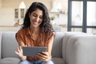 Dijital tablet kullanan genç bir kadının portresi, evdeki rahat koltukta oturması, boş yer. Neşeli bir milenyum kadını internette geziniyor, video izliyor, içeride arkadaşlarıyla görüntülü sohbet ediyor.