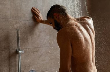 Çıplak Sakallı Adam 'ın portresi duştan zevk alıyor sıcak suyun altında duruyor, cesedi yıkıyor ve modern banyoda dinleniyor. Erkek Güzelliği, Vücut Bakımı ve Erkekler İçin Günlük Hijyen