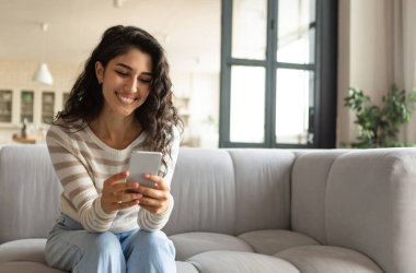 Milenyum Kafkasyalı kadın koltukta otururken akıllı telefon kullanıyor, mesajları kontrol ediyor, evde video görüşmesi yapıyor, boş yer arıyor. Sosyal medyada kapalı alanda cep telefonuyla paylaşım yapan güzel bir bayan.