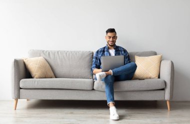 İnsanlar ve Teknoloji. Oturma odasındaki kanepede oturmuş klavyede daktilo yazan gülümseyen Arap bir adamın portresi. Neşeli adam internette geziniyor, internette sörf yapıyor, bedava fotokopi çekiyor.