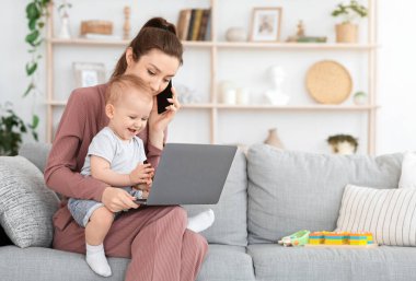 İş ve anneliği dengelemek. Genç anne telefonda konuşurken kucağında bebek, evde dizüstü bilgisayar, boş yer.