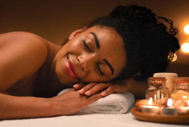 Aromaterapi tabağının yanındaki kaplıcada uyuyan neşeli siyahi kadının yakın çekimi.