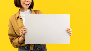 Vay canına. Reklam için beyaz tahta tutan heyecanlı bir kadın ve ağzı açık büyük boş bir levhaya bakıyor, sarı arka planda poz veriyor, mesaj için boş bir alan.