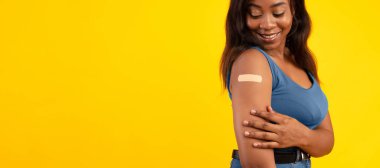 Afrikalı Amerikalı Kadın, Covid-19 'a karşı aşılandı. Sarı Arkaplan' ın üstünde duran antiviral aşı sonrası kolunu bandajla sardı. Stüdyo Çekimi