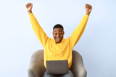 Zaferin sevinci. Heyecanlı Afrikalı Amerikalı Adam dizüstü bilgisayara bakıyor ve Gri Arkaplan Üzerine Oturarak Kazanan Oyun 'u Kutluyor. Başarı ve Şans, Büyük Çevrimiçi Haberler