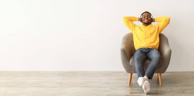 Siyahi Milenyum Adamı, kablosuz kulaklıkla müzik dinliyor. Gri arka planda gözleri kapalı oturuyor. Afro-Amerikan Adam Favori Şarkısını Seviyor İçerde Rahatlıyor