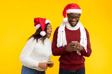 Vay canına başvuru formu. Yeni uygulamalı telefonlar kullanan, Noel Baba şapkası takan siyah bir çift, Smartphone 'un sarı arka planda duran cep telefonuyla mesajlaşırken sevgililerine bakan heyecanlı bir kız arkadaş.