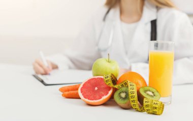Taze meyve, bir bardak meyve suyu ve mezura ile çevrili iken bir beslenme uzmanı notları gözden geçirip sağlıklı beslenme alışkanlıklarını ve beslenme tercihlerini parlak bir ortamda vurguluyor..