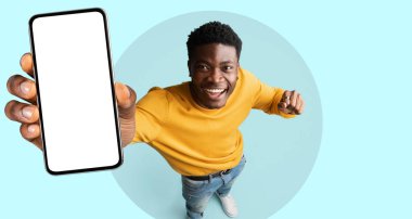 Bir adam mutlu bir şekilde duruyor, boş bir ekranla akıllı telefonu kaldırıyor, heyecanını gösteriyor. Açık mavi bir arka planda, pozitif enerji yayıyor ve bir neşe anı paylaşıyor..