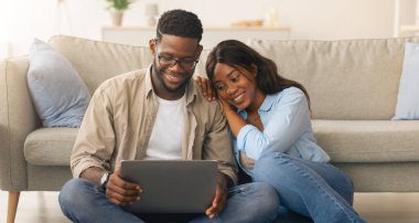 Genç siyahi çift birlikte dizüstü bilgisayar kullanıyor, internette sörf yapıyor ya da film seyrediyor oturma odasında yerde oturuyor, karısı kocalarının omzuna yaslanıyor. Evde bilgisayar kullanan milenyum eşleri