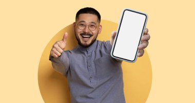 Gözlüklü genç bir adam elinde boş bir ekranla akıllı telefonu tutarken geniş bir gülümseme sergiliyor. Neşeli bir atmosferde, parlak bir geçmişi var..