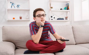 İzleyecek ilginç bir şey yok. Üzgün ve düşünceli genç bir çocuk uzaktan kumanda tutuyor ve televizyon izlerken sıkılmış görünüyor.