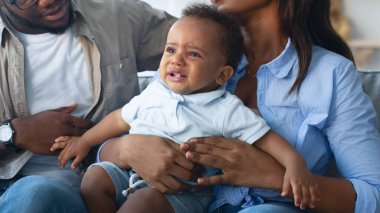 Genç Afrikalı Amerikalı bir kadının portresi, ağlayan siyah oğluyla birlikte evdeki kanepede oturuyor, küçük bebeği kucaklıyor ve sakinleştiriyor, sinir krizinden yorulmuş, gözlüklü bir adam oğlunu teselli etmeye çalışıyor.