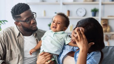 Ebeveynliğin zorlukları işte. Afro-Amerikalı ebeveynler ağlayan bebeği sakinleştirmeye çalışıyor, baş ağrısı çeken zenci kadın oturma odasındaki kanepede mızmız oğluyla oturuyor. İlk çocuk