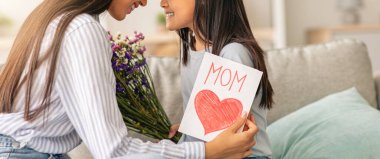 Anneler günün kutlu olsun. Sevimli Asyalı kızı annesini çiçekler ve tebrik kartı ile selamlıyor. Kanepede otururken alınlarına yapışıyor ve dokunuyor. Boşlukları kopyalıyor.