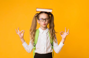 Sakin ol, okula git. İlkokul Öğrencisi Kız Meditasyon Tutan Kitap On Head On Yellow Background. Boş Alan