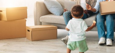 Mutlu Afrikalı çocuk yeni bir dairede koşuyor ebeveynlere bakıyor, küçük oğlu taşınma gününde evi keşfediyor, insanlar kutuları açıyor, çocuklar ve aile ipoteği taşınıyor.