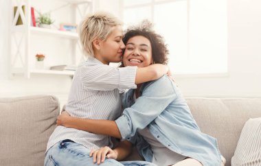 İki kadın, yumuşak ışık ve rahat dekorla çevrili rahat bir kanepede samimi bir anı paylaşıyor. Kahkaha ve sıcaklık sevinçle kucakladıkları atmosferi dolduruyor..