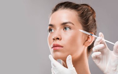 Gri stüdyo arka planında güzel bir kadın güzellik iğnesi yaptırıyor. Yakın plan, kopyalama alanı.