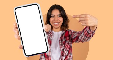 Neşeli genç bir kadın parlak bir arka plana karşı duruyor, boş bir ekranla akıllı telefonunu işaret ederek, izleyicileri onunla ilgilenmeye davet ediyor, heyecan hissi sergiliyor..