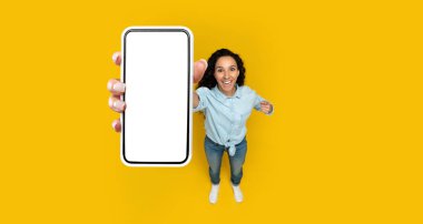 Akıllı bir telefonla ayakta duran bir insan, canlı sarı bir arkaplana sevinçle gülümsüyor. Bu sahne, paylaşım anları için mükemmel bir çevredeki coşku duygusunu yakalar..