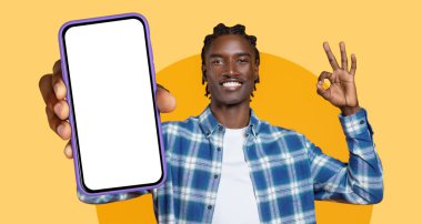 Gülümseyen bir adam, tamam işareti yaparken akıllı telefona boş bir ekran sunar. Arka plan parlak ve renkli, canlandırıcı bir atmosfer yaratıyor..