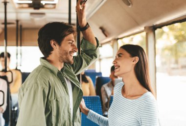 İki genç yetişkin şehir otobüsünde neşeli bir sohbete girişiyor. Adam bir direğe tutunurken aynı zamanda gülümseyen kadına gülümsüyor. Otobüsün içi parlak ve canlı..