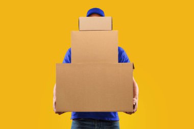 Paketler teslimat. Tanımlanamayan Kurye Adam elinde bir sürü büyük karton kutu tutarak sana paketler teslim ediyor. Stüdyoda durmuş sarı arka planda poz veriyor. Posta Servisi Konsepti