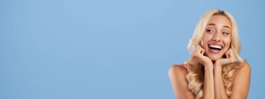 Mevcut kavram. Şirin, güler yüzlü, şık, sarışın bir kadının portresi alışveriş çantasına bakıyor, el ele tutuşuyor ve içi boş kağıt paketler veriyor. Model tasarımı için, mavi stüdyo arka planı, afiş.