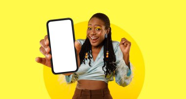 Neşeli bir kadın elinde akıllı bir telefonla poz veriyor. Gülümsüyor ve heyecanını dile getiriyor. Parlak sarı arka plan onun hayat dolu enerjisini ve pozitif enerjisini arttırır..