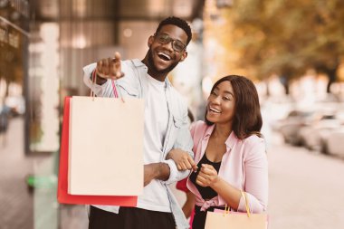Harika bir teklif. Heyecanlı genç Afrikalı eşler kaldırım kenarında parlak alışveriş torbalarıyla dikiliyorlar. Duygusal adam mağazanın camını işaret ediyor. Çift mevsimlik indirimlerden ve anlaşmalardan zevk alıyor.