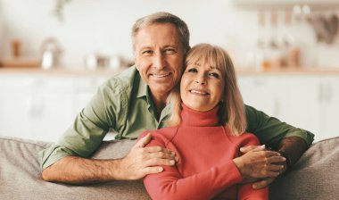 Mutlu son sınıf çifti koltukta oturmuş kameraya gülümsüyor ve evde poz veriyor. Evlilik ve Mutluluk, Emeklilik ve Aile Hayatı Romantik İlişki Olgunluk Çağı Kavramı