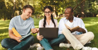 Neşeli çok ırklı öğrenciler konuşuyor ve dizüstü bilgisayar kullanıyor, üniversite kampüsünde dinleniyor ve açık hava derslerine ya da sınavlara hazırlanıyor.