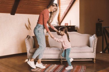 Eğlence Faaliyetleri Konsepti. Tüm vücut uzunluğu pozitif bir annenin kızıyla dans etmesi ve dans etmesi. Kız ve anne oturma odasında aileleriyle eğleniyor.