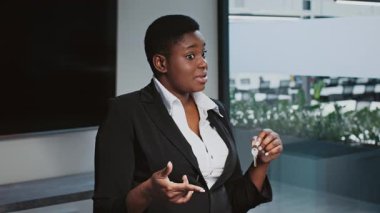 Kurumsal bir ofiste, genç bir Afrikalı Amerikalı kadın anahtarlarını tutarken güvenli bir şekilde stratejileri tartışıyor, bir iş lideri olarak rolünü sergiliyor. Modern çevre profesyonelliği vurguluyor.