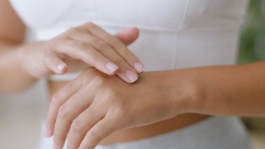 Sıcak bir ev ortamında, genç bir Asyalı kadın eline nemlendirici sürüyor, cilt bakımına odaklanıyor. Bu şımarık an, onun güzelliğe ve kendine olan bağlılığını vurguluyor..