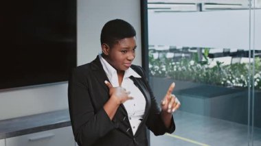 Profesyonel kıyafetli genç bir Afrikalı Amerikalı kadın, yeşillik dolu çağdaş bir ofis ortamında tutkulu bir şekilde şirket stratejisini tartışıyor..