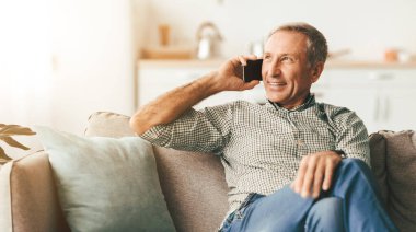 Cep telefonuyla konuşan mutlu son sınıf öğrencisi evde koltukta yan yana oturuyor. Kapalı alanda cep telefonu sohbeti yapan erkek iletişimi. Modern İletişim, İnsanlar ve Gadget Kavramı