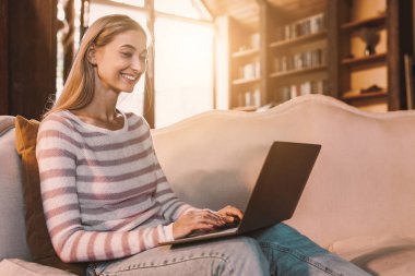 Oturma odasındaki kanepede dizüstü bilgisayar kullanan neşeli bayanın portresi, bedava fotokopi alanı. İnternette arkadaşlarıyla sohbet eden mutlu bir kadın, klavyeye yazı yazan, evden çalışan serbest çalışan bir kadın.
