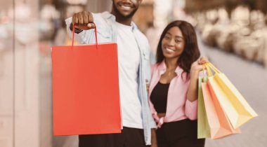 Alışveriş, Perakende ve Tüketim Konsepti. Boş uzay modeliyle alışveriş torbası tutan mutlu Afro-Amerikan çiftin portresi. Alışveriş merkezinin önünde duruyorlar. Gülümseyen adam ve bayanın alışverişi