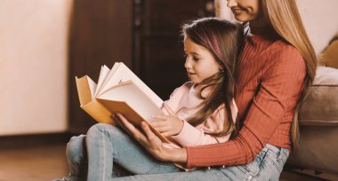 Profil yan görüntüsü: Mutlu Gülümseyen Anne ve Sevimli Küçük Kız 'ın birlikte kitap okuduğu evde koltuğa yaslanıp birlikte vakit geçirdikleri. Yatma zamanı Hikayesi Konsepti