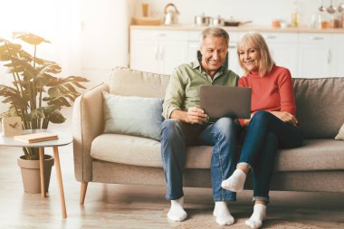 Neşeli Son Sınıf Eşleri dizüstü bilgisayar kullanarak Onilne Filmi 'ni izliyor ya da evdeki koltukta oturmuş interneti inceliyor. Yaşlılar ve Gadget 'lar, Modern Emeklilik Yaşam Tarzı Konsepti
