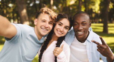 Çok ırklı öğrenci arkadaşlar selfie çekiyorlar, işaret diliyle işaret veriyorlar, baş parmağını kaldırıyorlar, kampüste poz veriyorlar. Gençler üniversiteye girdikleri için mutlu.