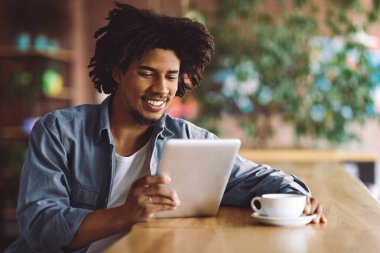 Kafe 'de dijital tablet ve kahveyle rahatlayan genç Afrikalı Amerikalı adam sosyal medyaya göz gezdiren ya da kafeteryada dinlenirken modern Gadget' ta haber okuyan siyah adam.