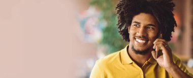 Telefon var. Kapalı alanda cep telefonuyla konuşan gülümseyen siyahi bir adamın yakın plan portresi, telefonda hoş sohbetler yapan ve başka yöne bakan mutlu Afrikalı genç Amerikalı adam, seçici odaklanma.