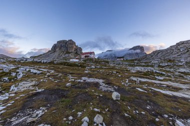 Tri Cime Doğal Parkı 'ndaki Rifugio Antonio Locatelli' de sabah huzuru. Torre Di Toblin gururla arkasında duruyor, sonbahar gündoğumunun yumuşak parıltısı tarafından öpüldü. Doğanın sakin zarafeti sergileniyor