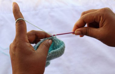 Kafkasyalı bir kadın elleri, iğne ve açık mavi iplik kullanarak mobil yün bir çanta örüyor.